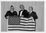 John Joseph Moakley, William M. Bulger, and a veteran holding an American flag at a veterans' event by unknown